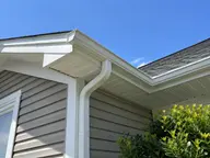 A clean white gutter and downspout on a roof corner