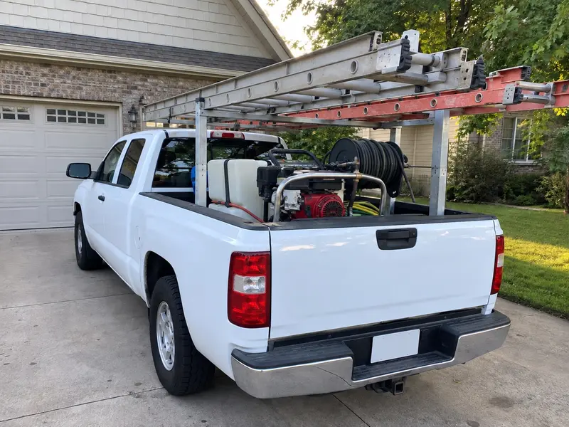 A white pickup with ladders on a rack and a pressure washer in the bed